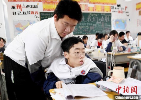 朱金祥(左)把鐘華強(qiáng)放到課堂座位上后，都要把他擺正好，確認(rèn)安全后才回到自己的座位上。 卓忠偉 攝