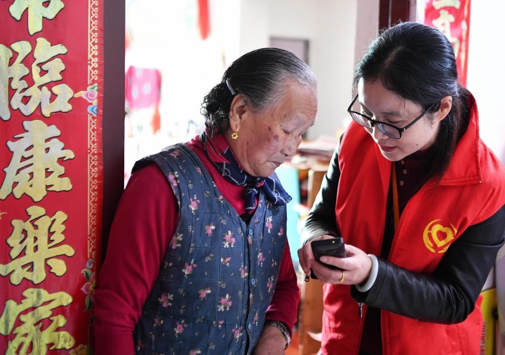 在福州市長樂區(qū)航城街道籌岐村，智慧養(yǎng)老平臺派駐社區(qū)的助老員（右）在為老人陳鳳英（左）講解養(yǎng)老定制手機的用法（2021年11月26日攝）。新華社記者 魏培全 攝