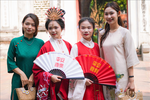身穿古裝的中國(guó)游客和身穿越南傳統(tǒng)服飾奧黛的越南青年在文廟門前合影。