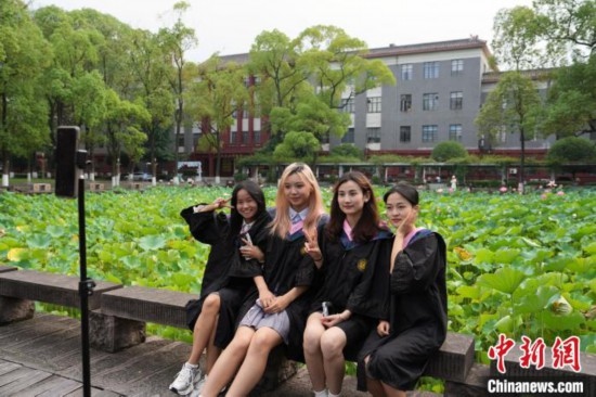 6月19日，時值一年畢業(yè)季，四川大學望江校區(qū)荷花池里的荷花盛開，成為了畢業(yè)生們的打卡圣地，吸引了眾多畢業(yè)生拍照留念。圖為畢業(yè)生在荷花池邊拍照留念。中新社記者 安源 攝