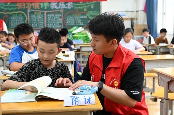 鄭州市二七區(qū)暑托班的志愿者輔導(dǎo)孩子寫作業(yè)。人民網(wǎng)記者王玉興攝